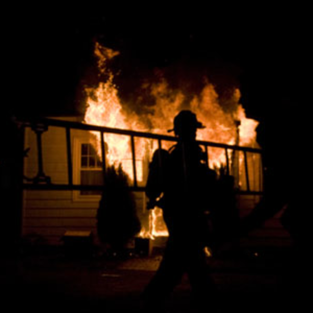 Certified fire investigator with a ladder in front of a house on fire